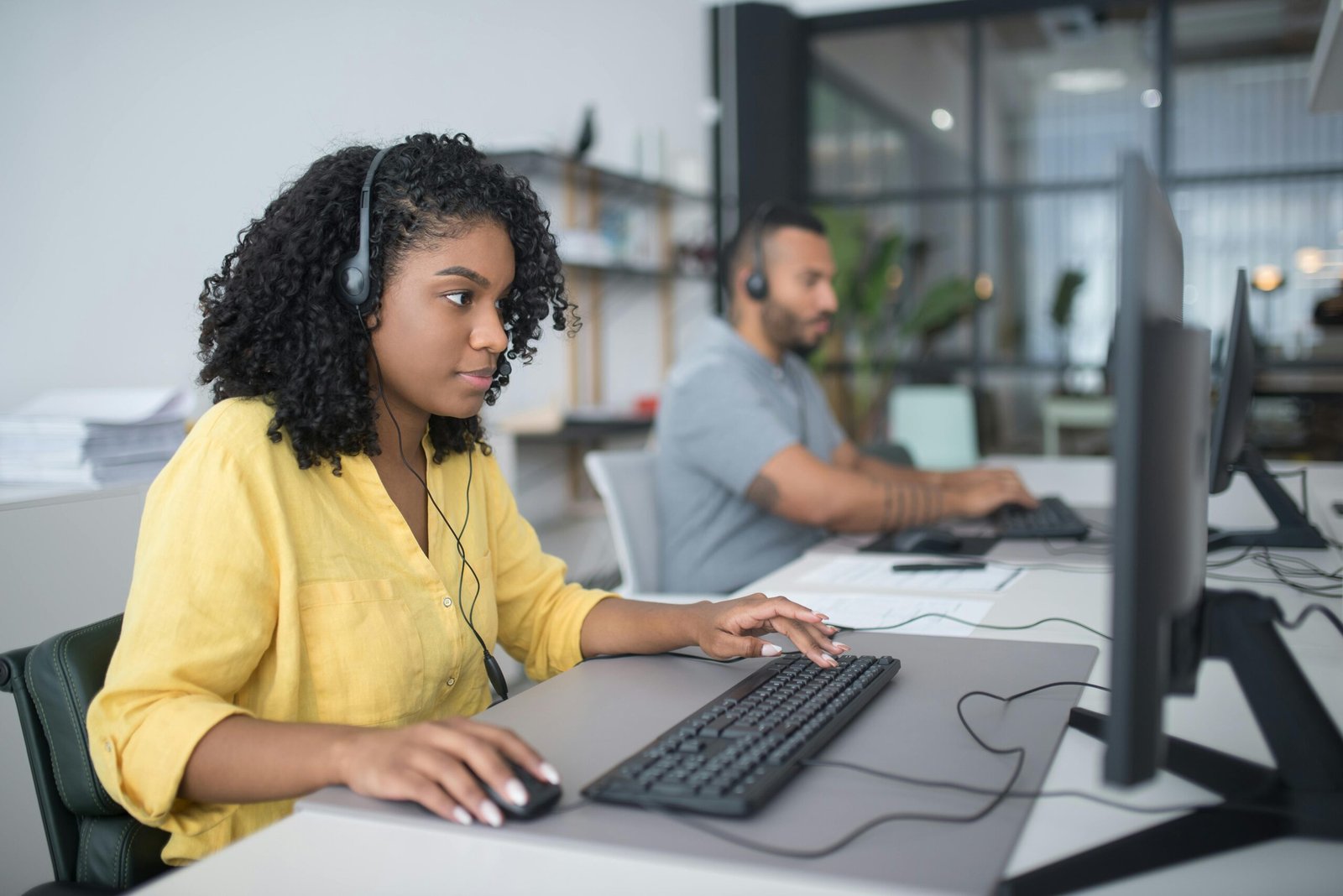 Two customer service agents working with headsets in a modern office setting.